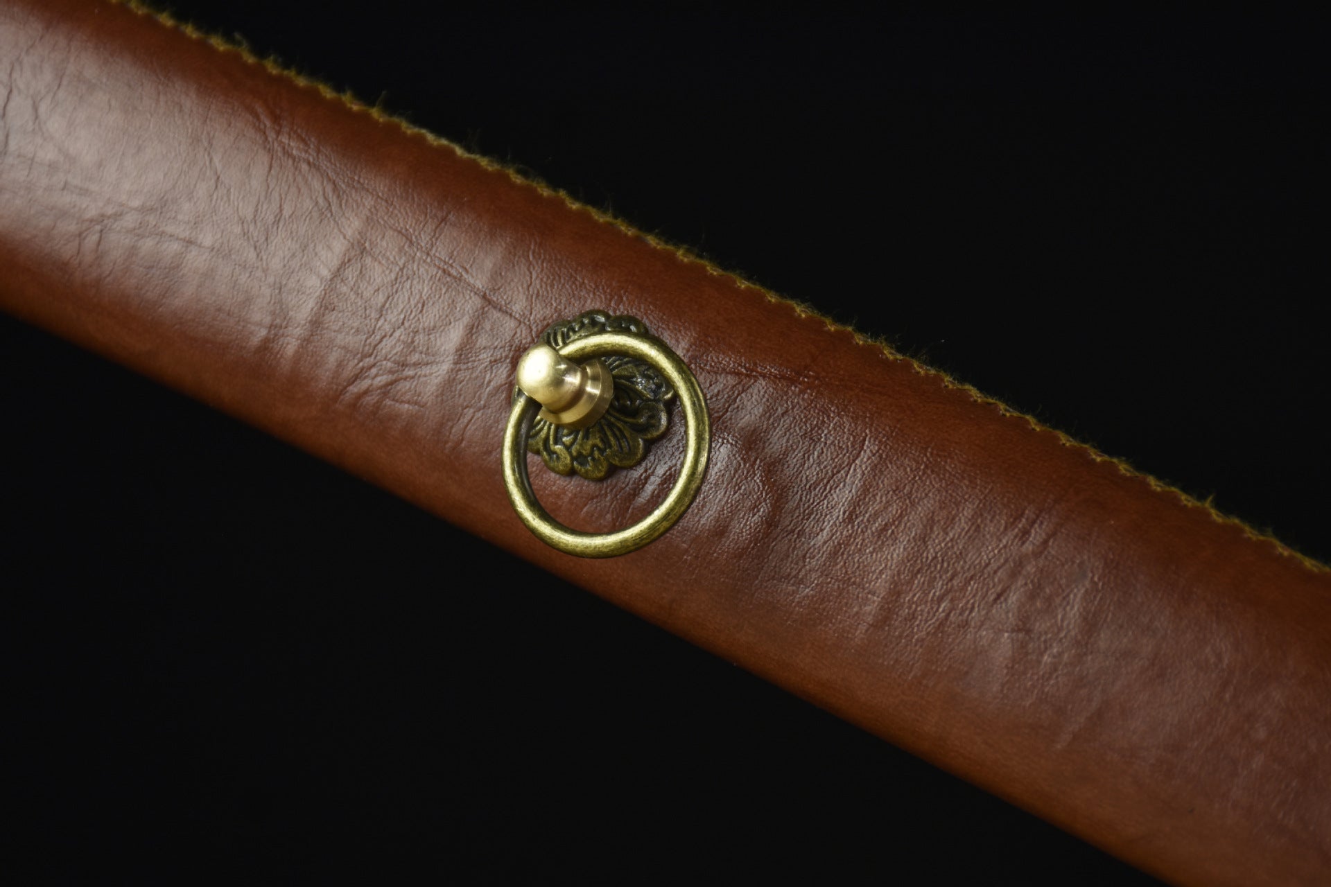 A close-up view of a brown leather katana scabbard on a black background