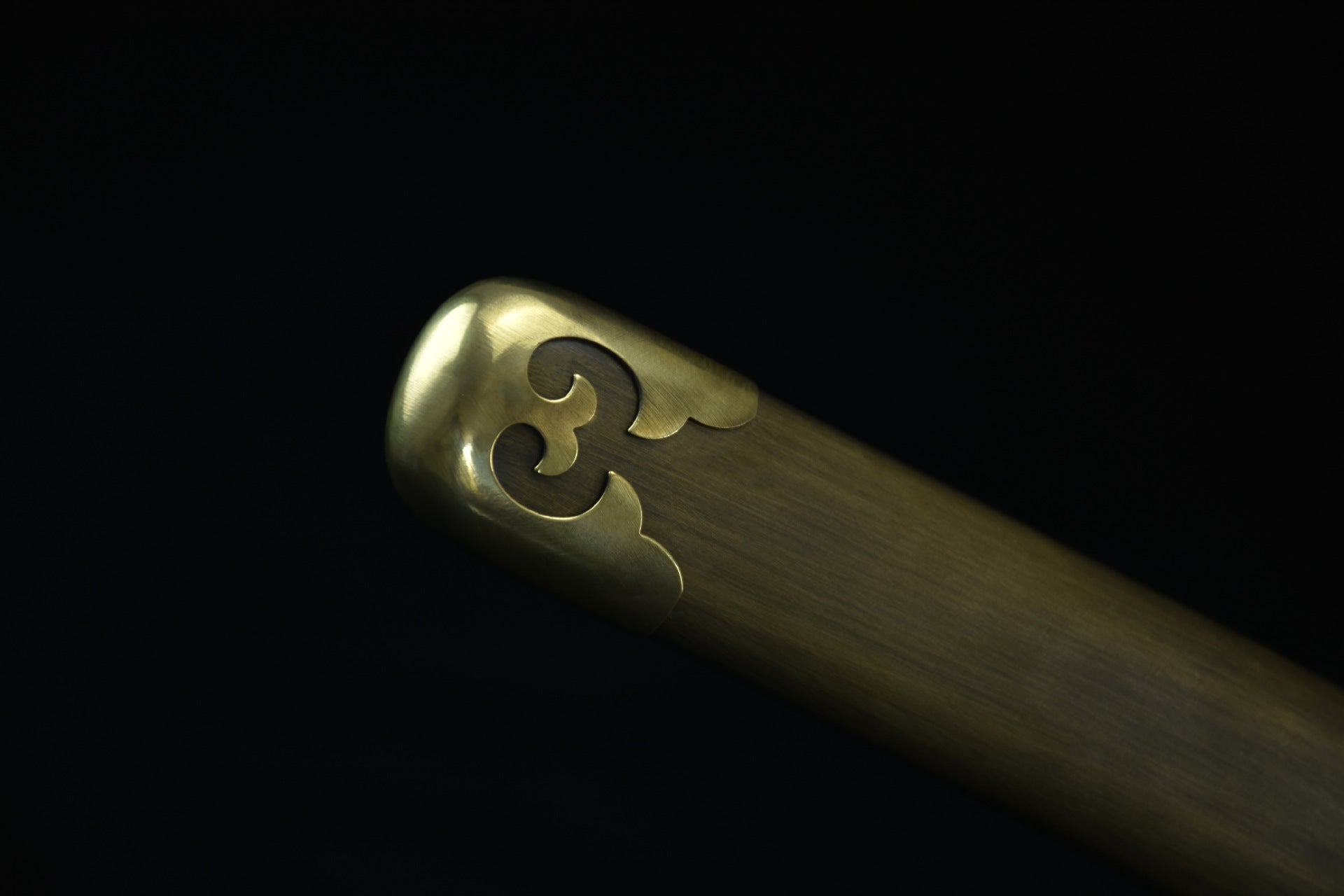 Close-up of the samurai sword saya tip, featuring intricate brass detailing and a decorative design.