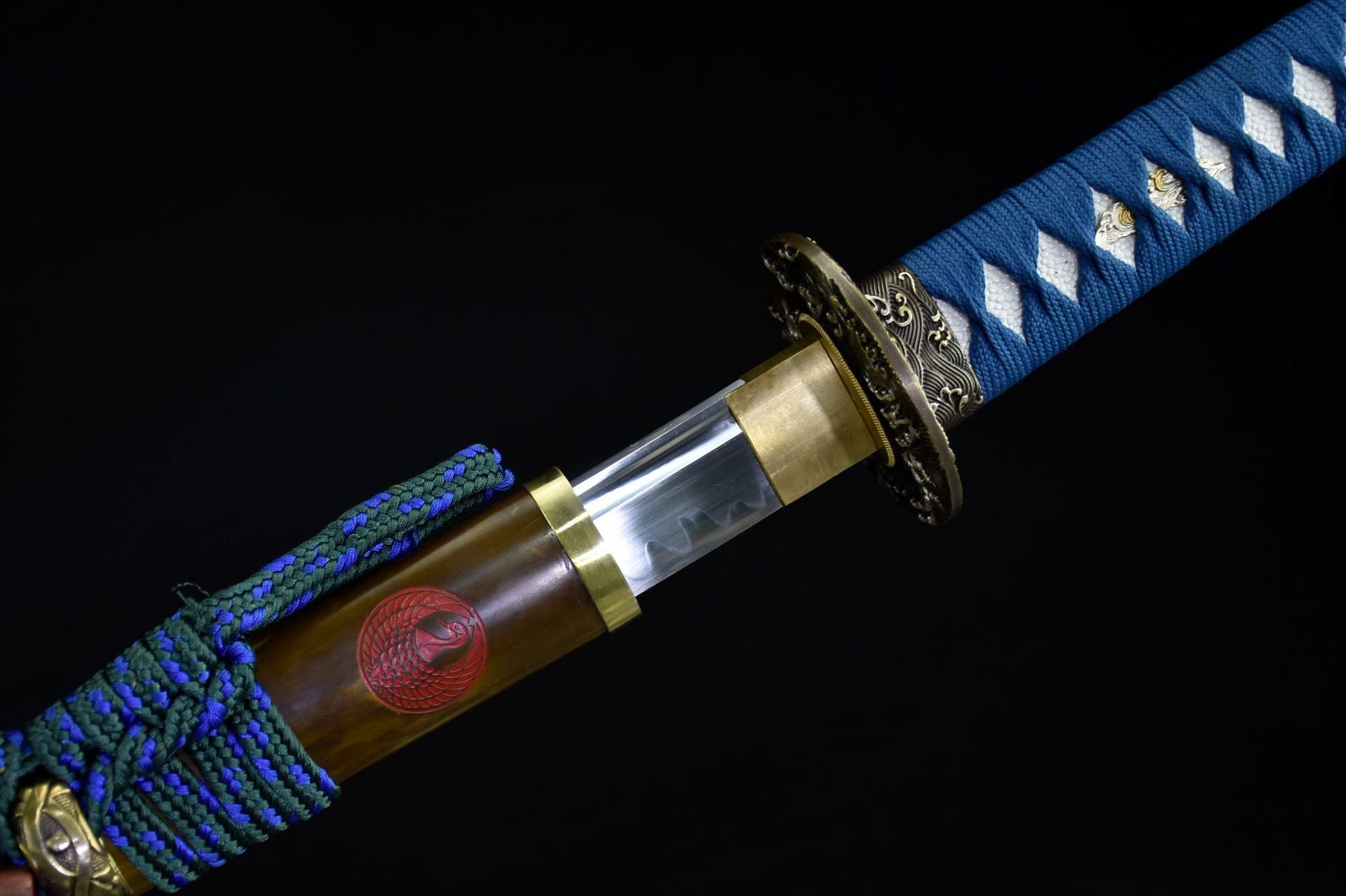 Close-up of the Ichiro Matsuru katana showing the polished blade with hamon, ornate tsuba, and decorated saya with a red emblem.