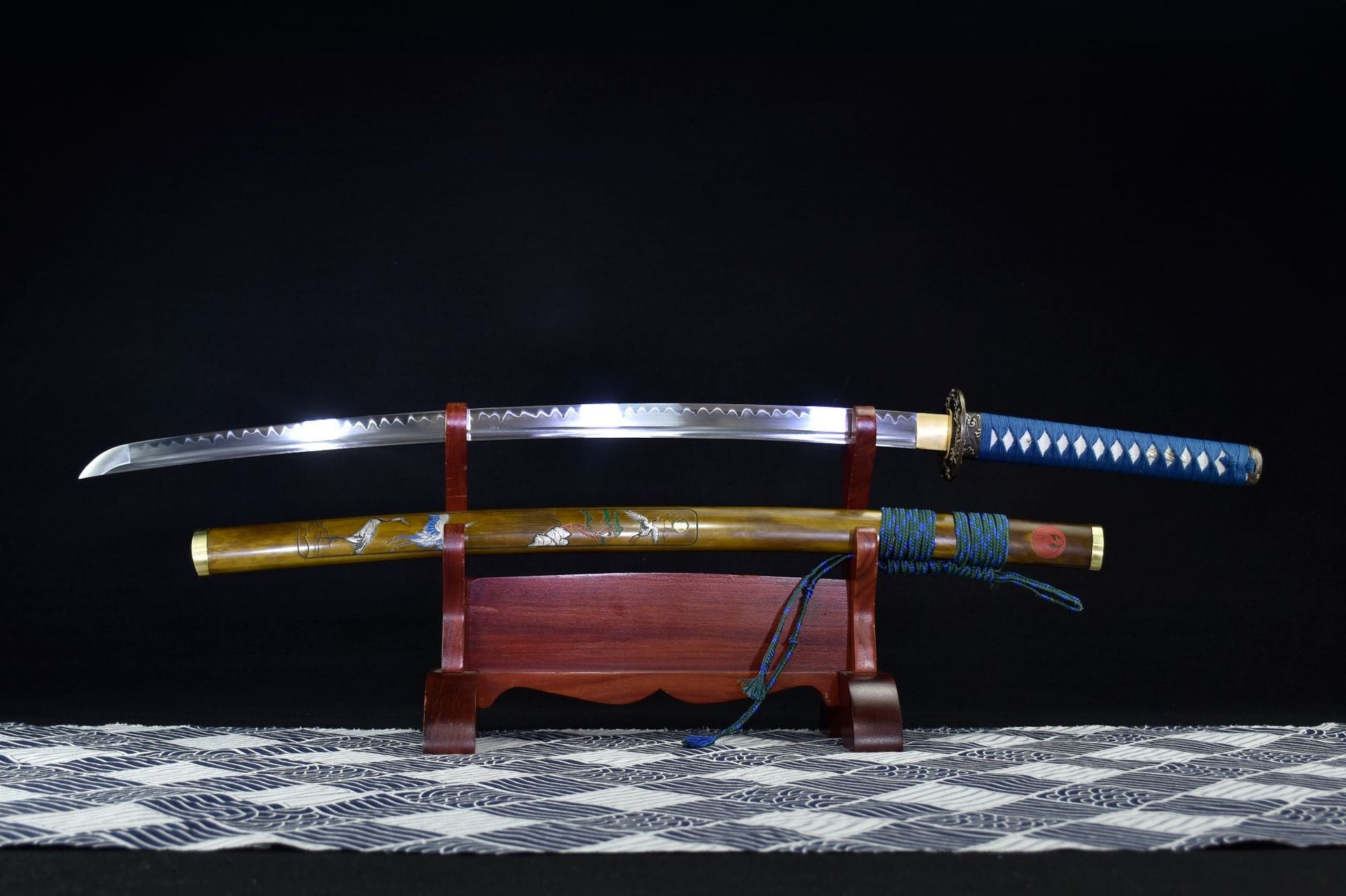 Ichiro Matsuru katana sword with a polished blade, blue wrapped handle, and decorative artistic sheath displayed on a wooden stand.