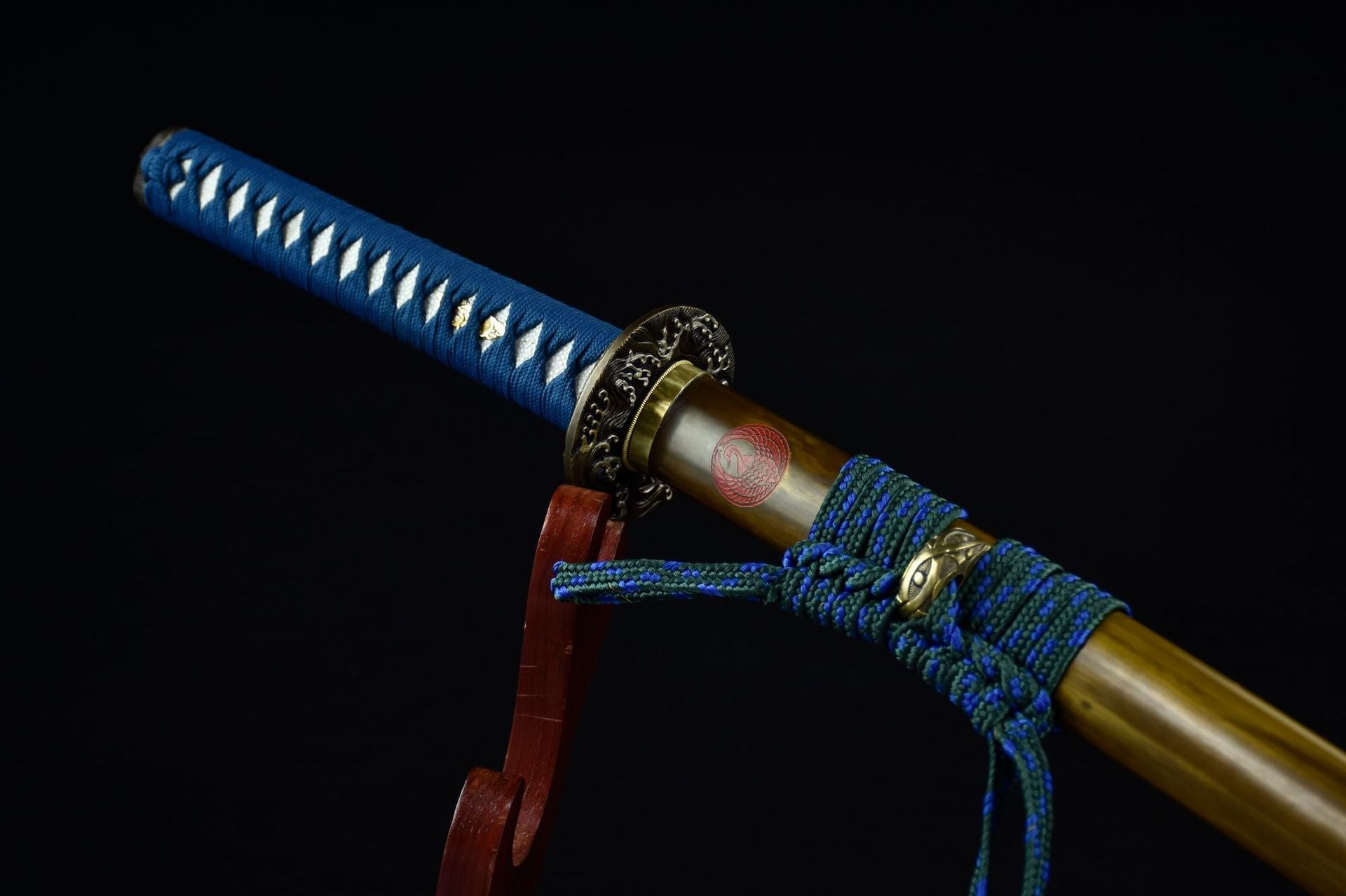 Close-up of the Ichiro Matsuru katana's tsuka with blue wrapping and ornate tsuba, paired with a saya featuring a red emblem and sageo cord.