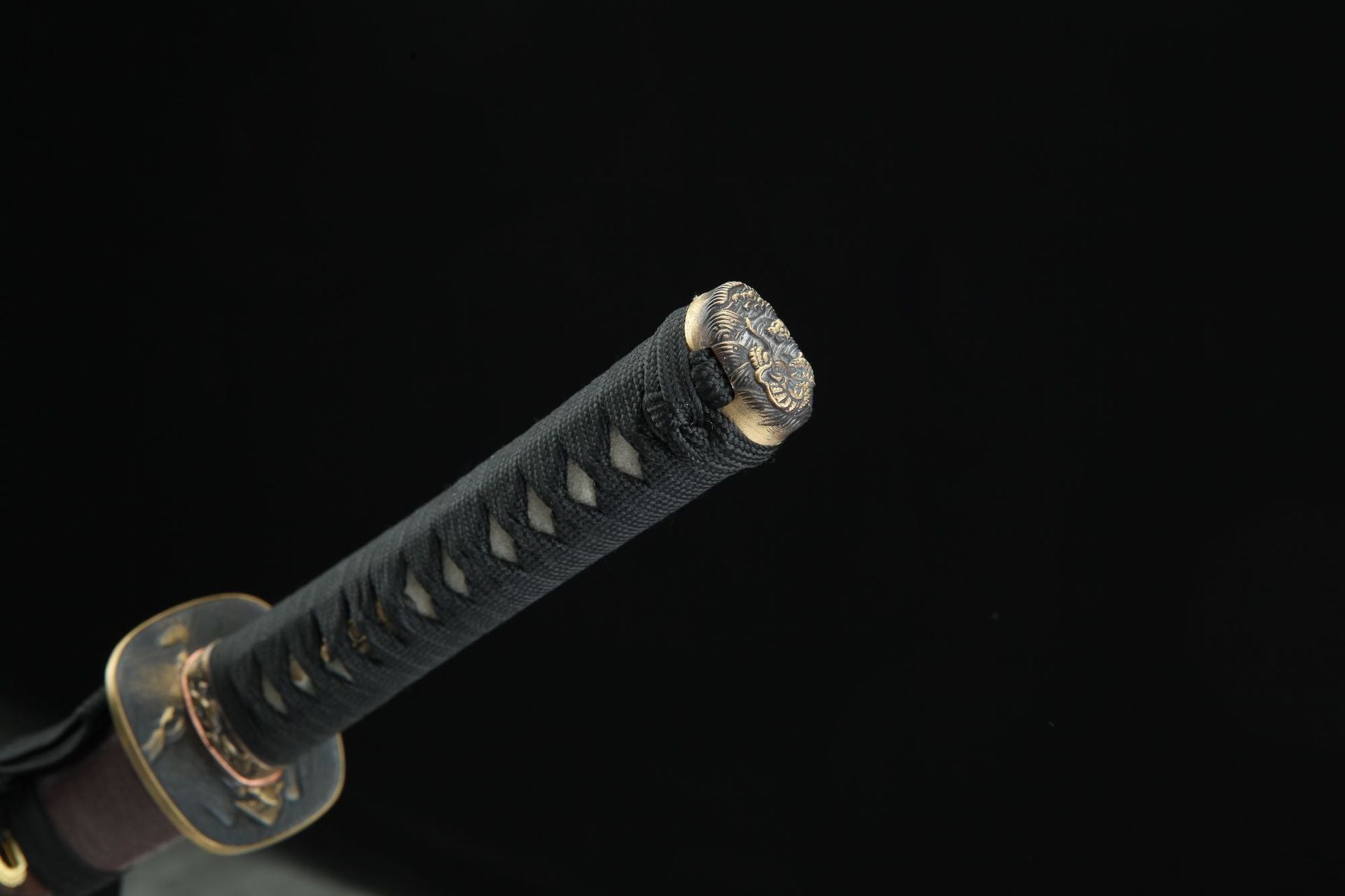 Close-up of the Jiang Tai Gong katana showing the decorative brass kashira with intricate patterns, black tsuka-ito wrapping, and white samegawa underneath.