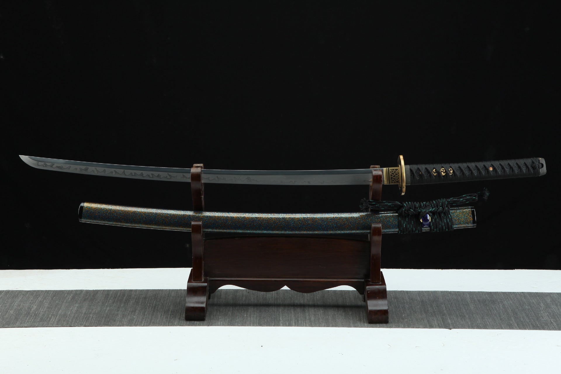 Magatama katana fully displayed on a wooden stand, showing the black blade, decorative saya, and intricate tsuka wrapping.