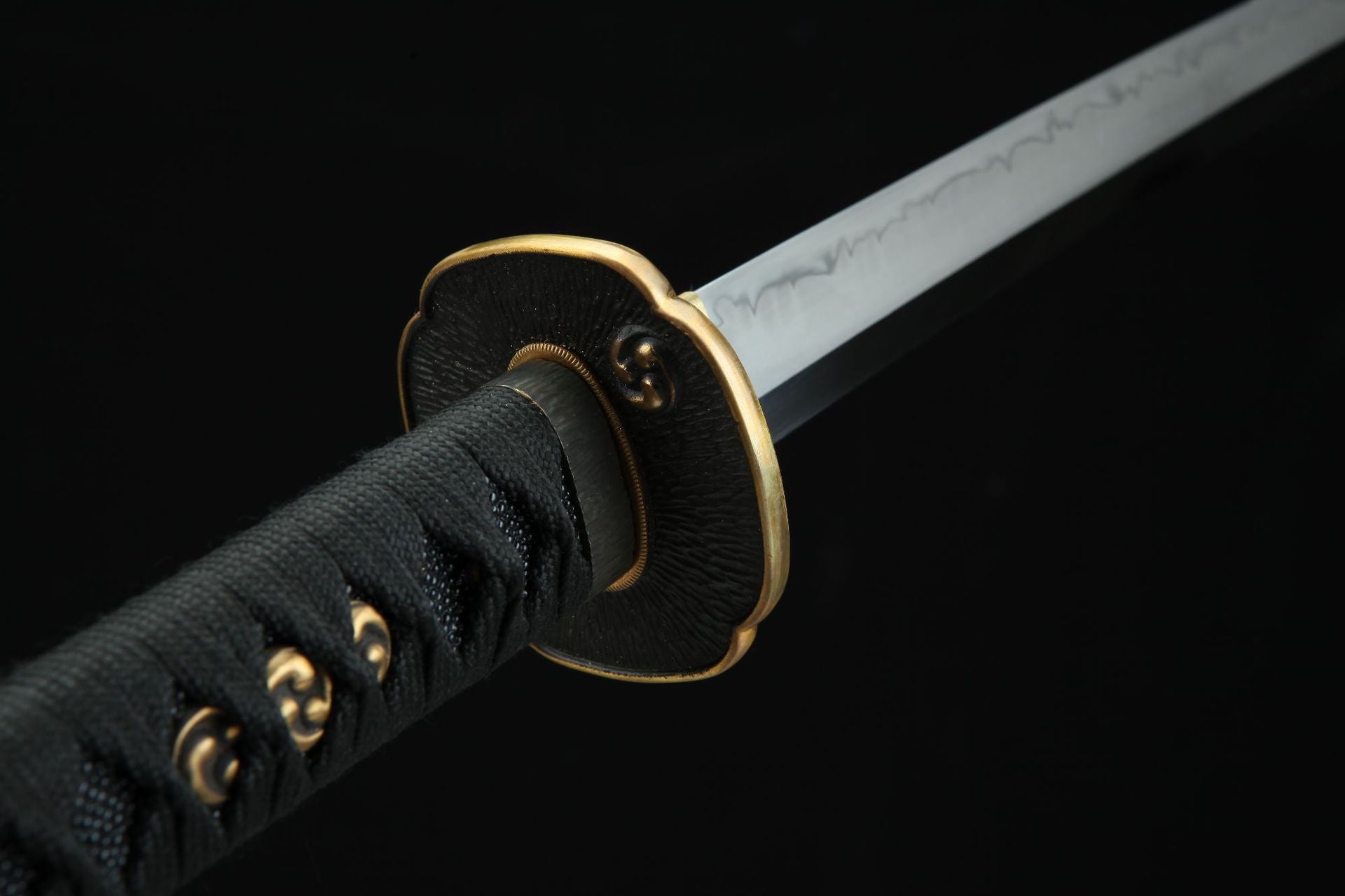 Detailed view of the Magatama katana handle and tsuba, featuring gold accents and a hamon pattern on the blade.