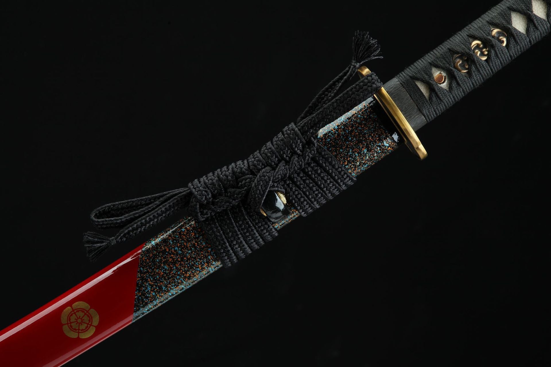Close-up of a samurai sword handle with black cord wrap, brass guard, and red lacquered scabbard featuring decorative floral design.