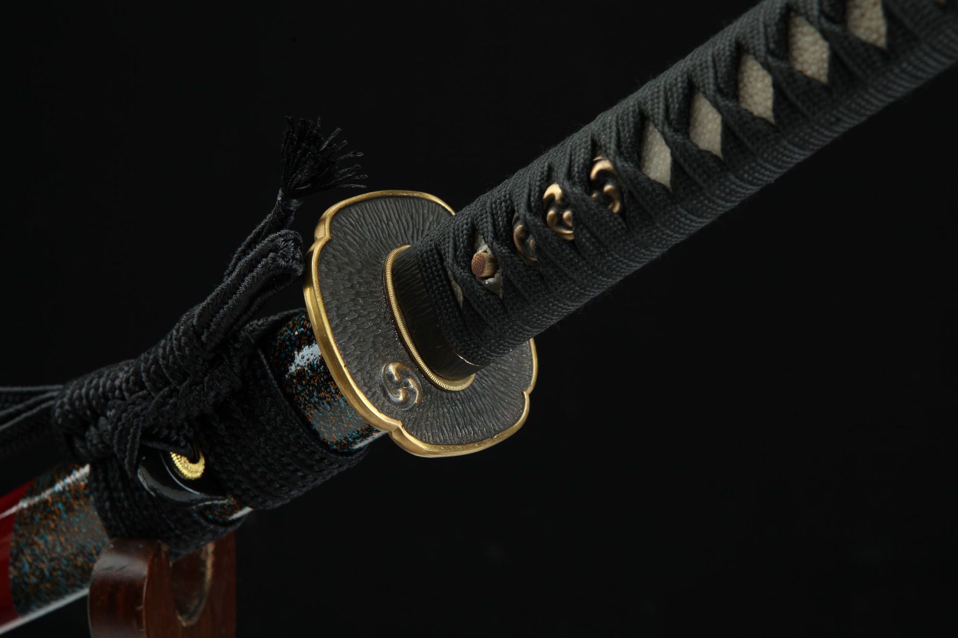 Close-up of a samurai sword handle featuring a brass tsuba and intricate black handle wrap, with decorative fittings.