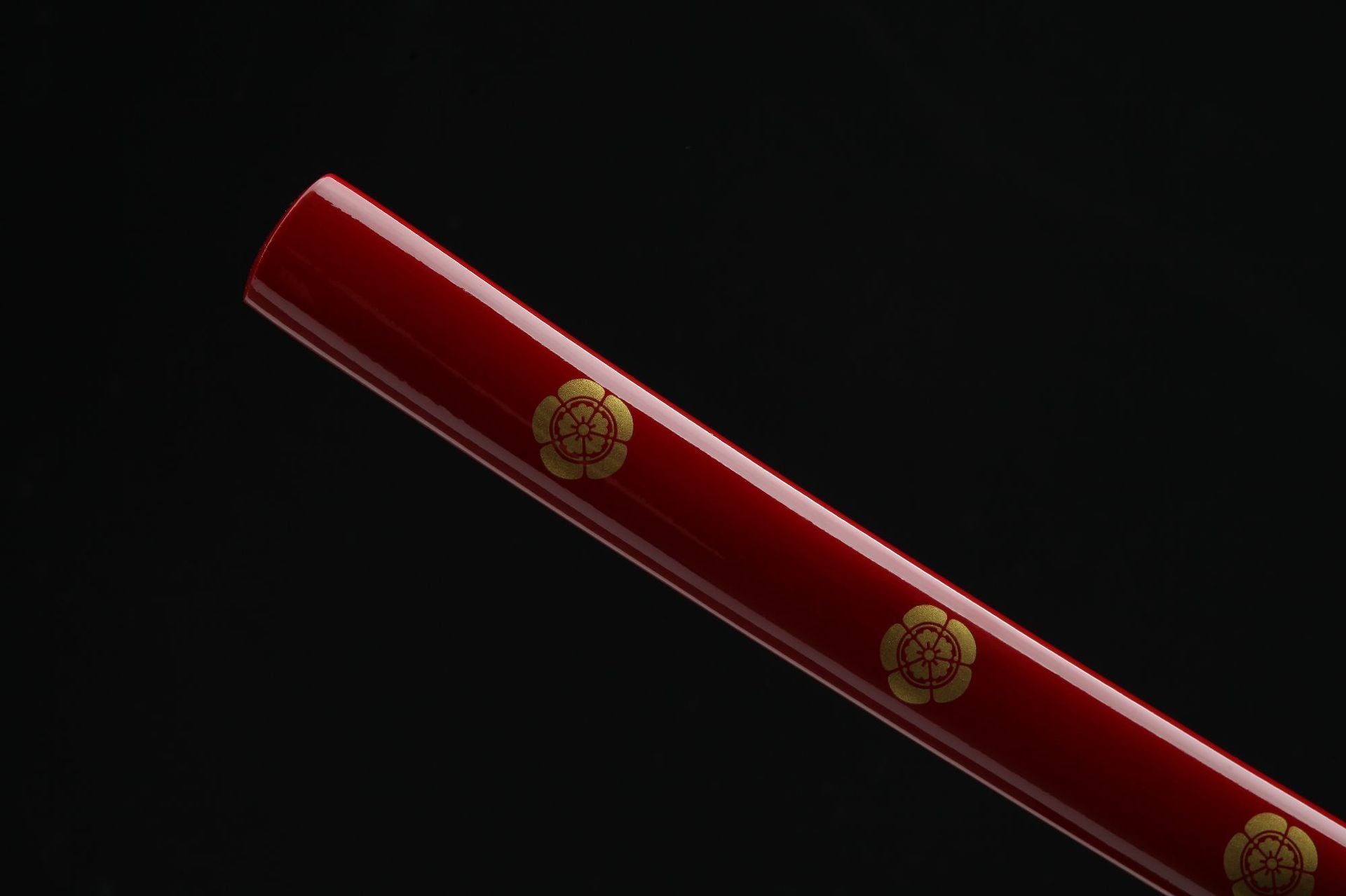 Close-up of the red saya (scabbard) of a samurai sword, featuring a gold flower pattern design.