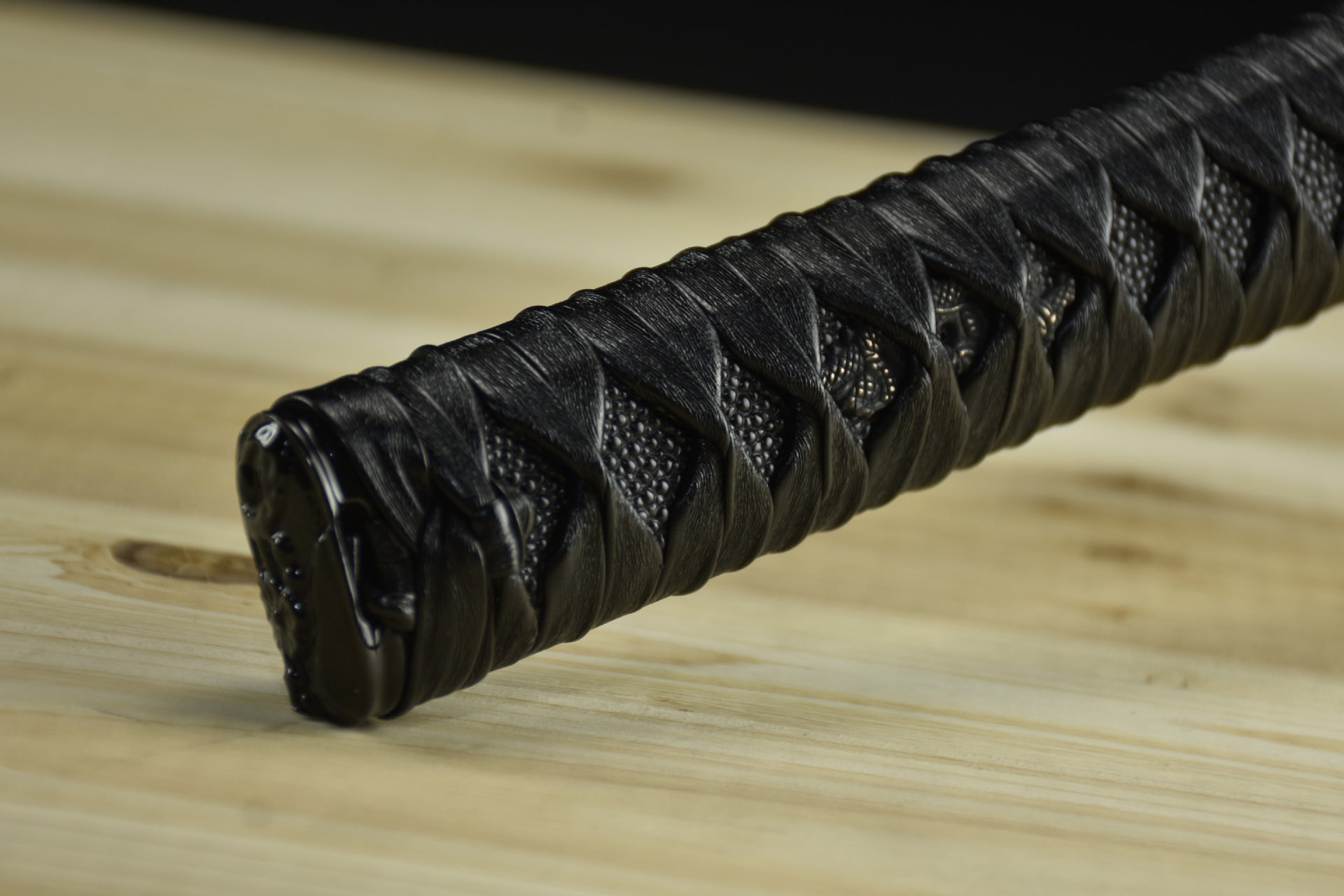 A close-up of a black tsuka and kashira of a Japanese katana.