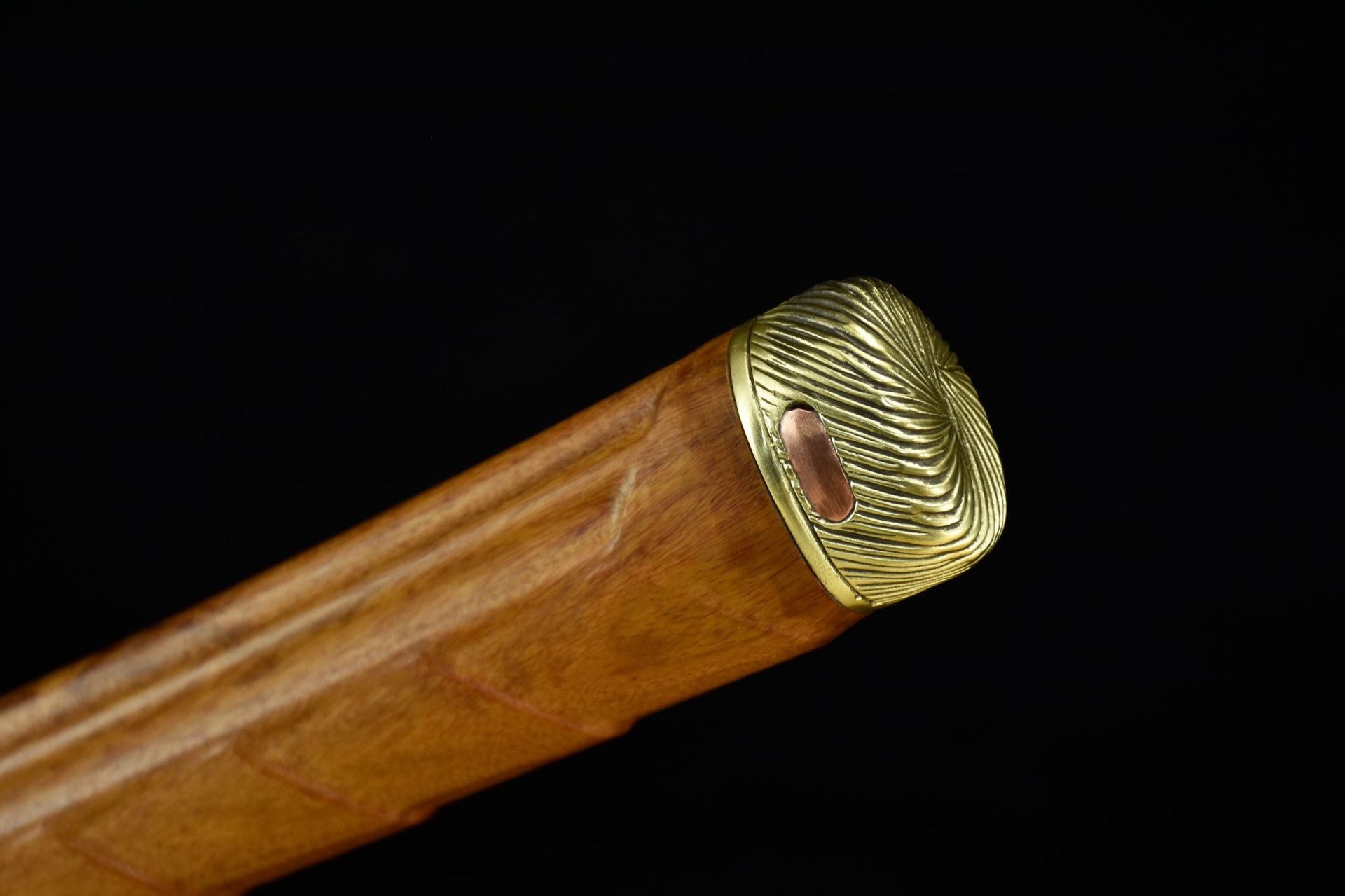 A close-up of a katana handle with a polished brass kashira, featuring intricate detailing and a smooth wooden finish.