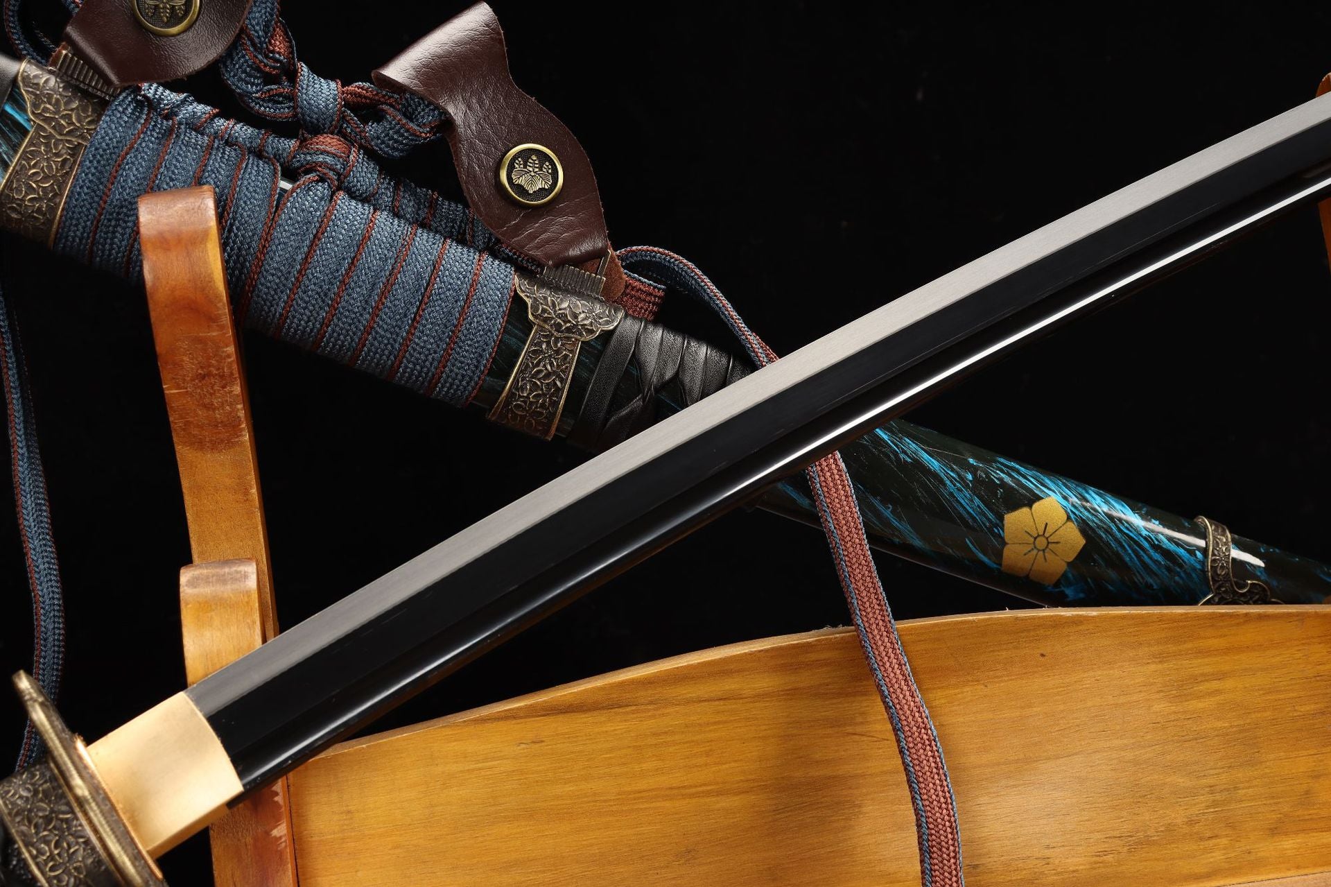 Closeup of a tachi blade with a polished edge, blue and gold scabbard, and intricate sageo wrapping.