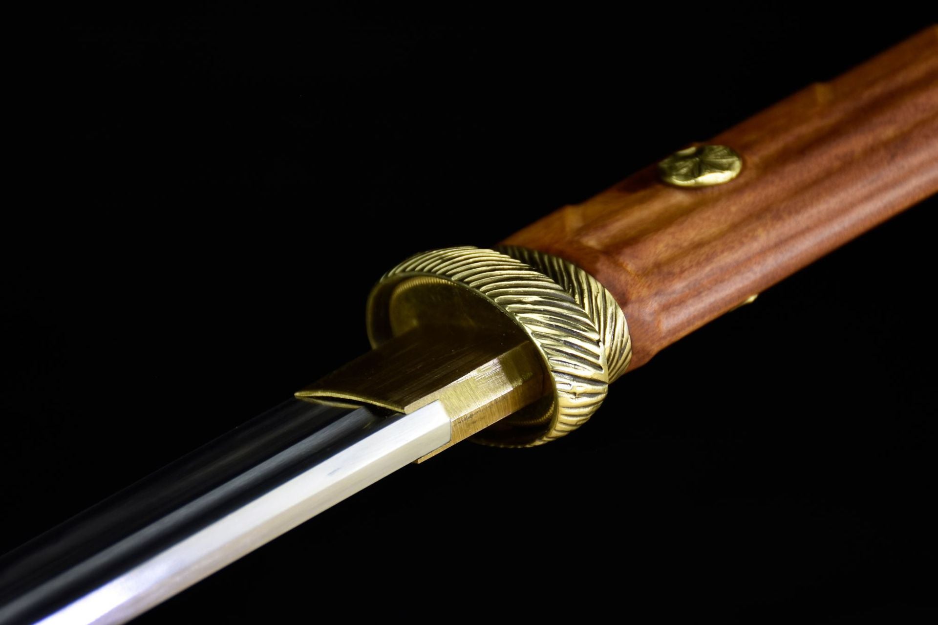 A close-up of a katana featuring a brass habaki, an intricately engraved tsuba, and a polished wooden handle, highlighting refined details.