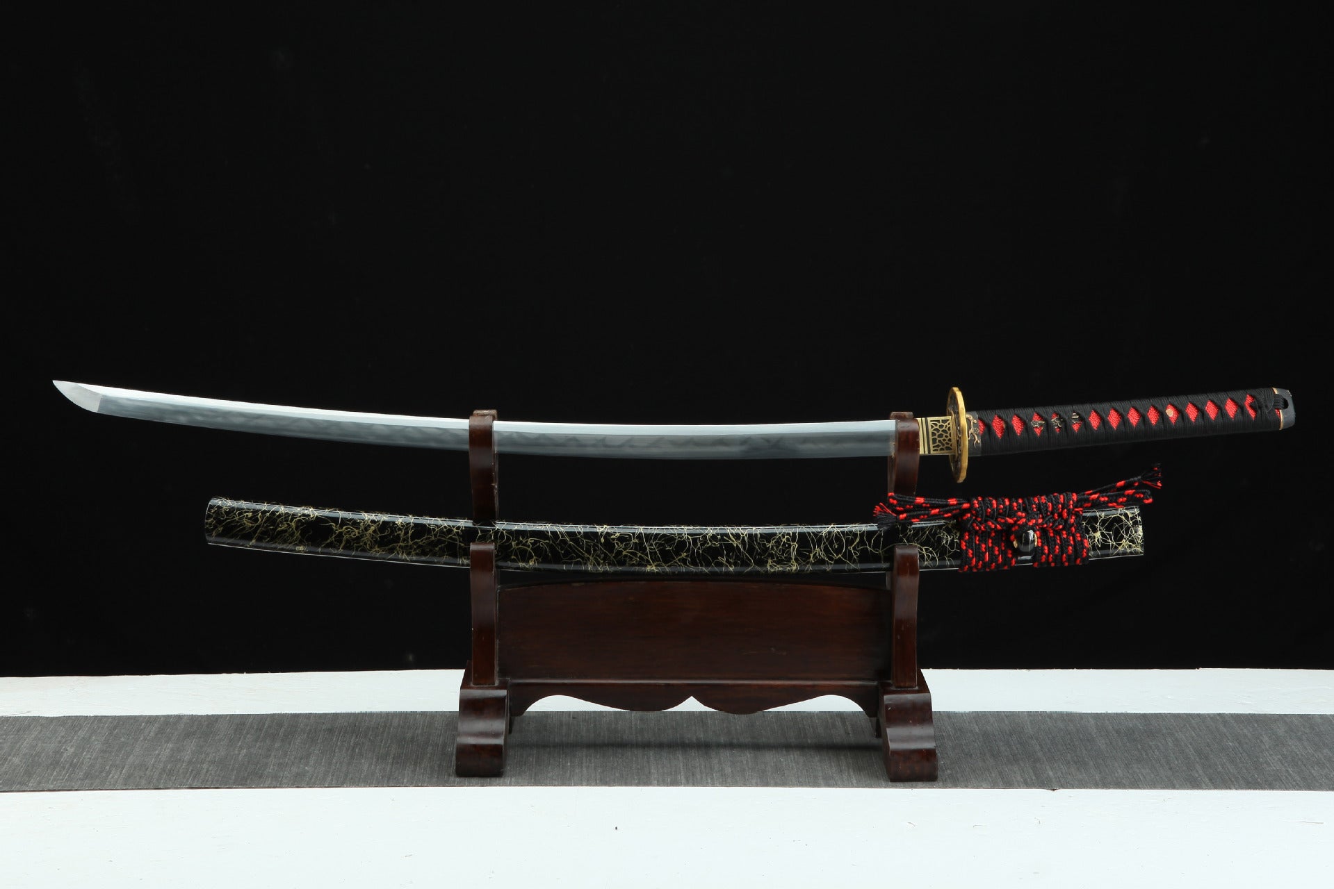 Japanese katana sword with a black and red cracked design saya, featuring a polished blade and intricate tsuka with black and red wrapping.