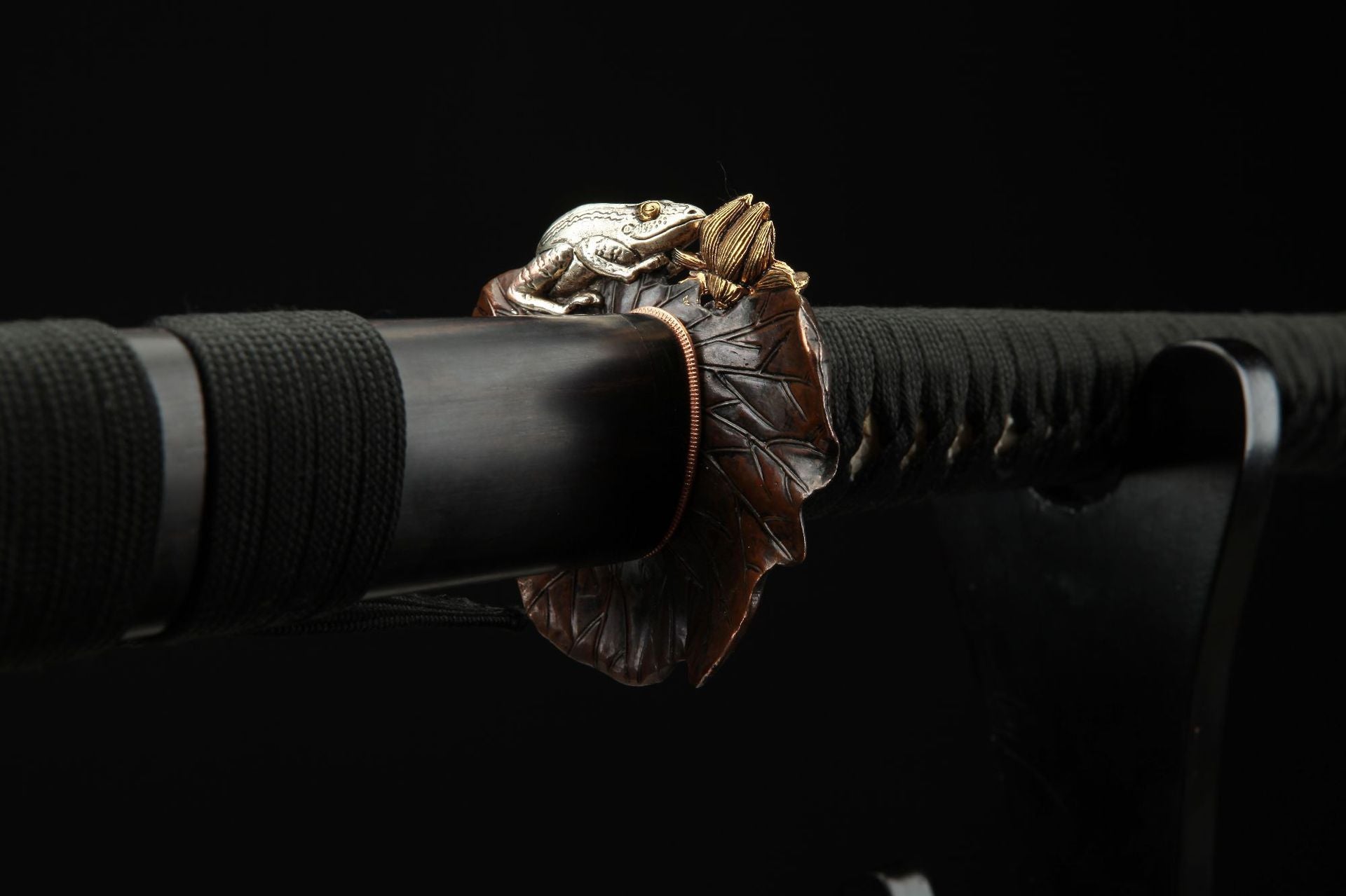 Reverse side view of the Lotus katana's tsuba, featuring a detailed carving of a lotus leaf and toad.