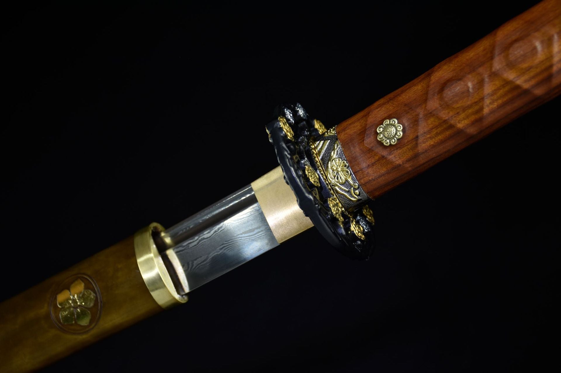 Fuchi of Moonlit Sakura samurai sword, highlighting detailed gold sakura motifs on dark metal.