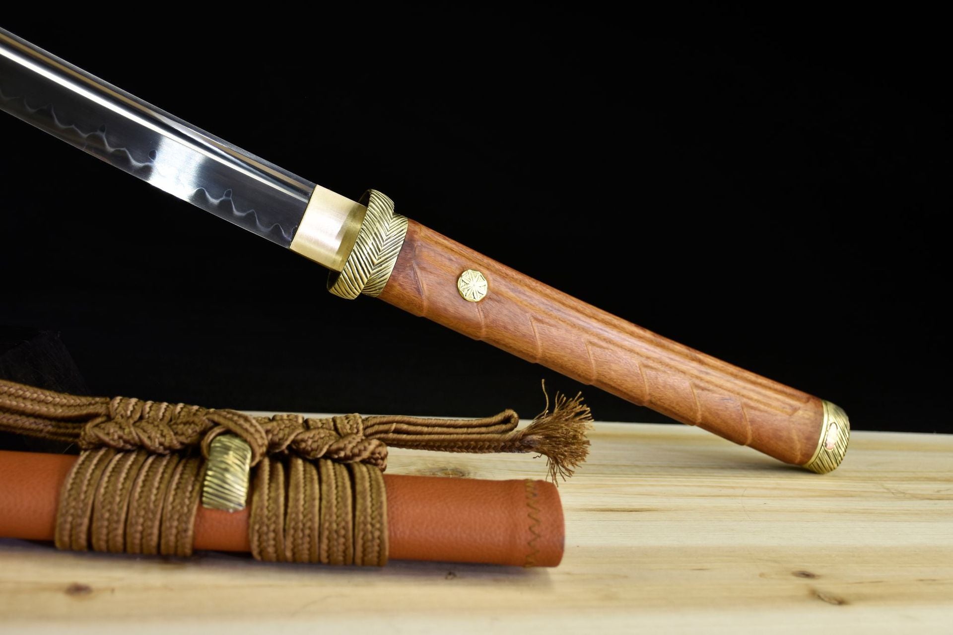 A polished katana blade with a wooden handle and brass fittings, paired with a tan scabbard wrapped in decorative cord, showcasing traditional design.