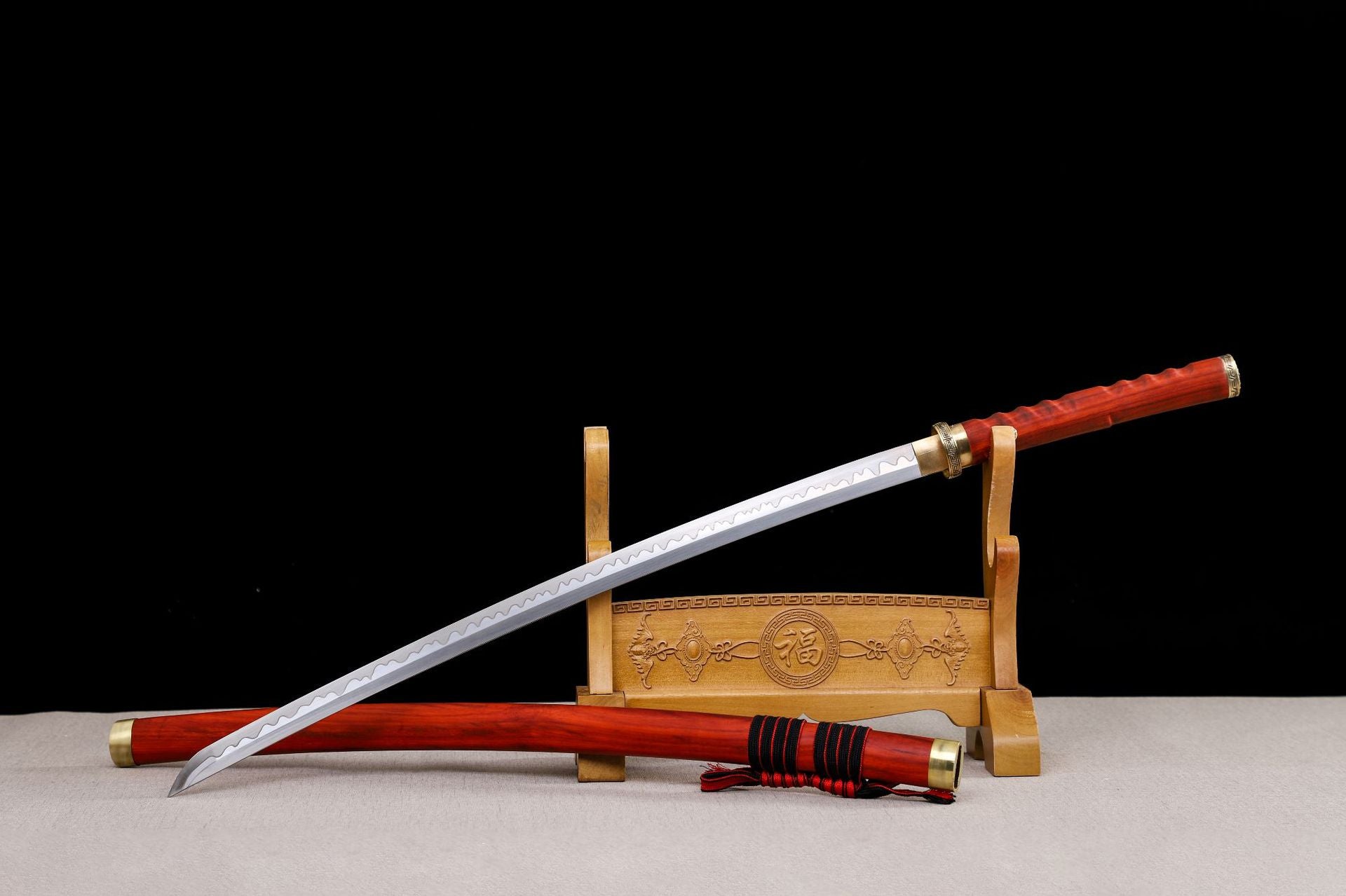 Full display of a Japanese katana with a red rosewood saya, polished blade featuring a wavy hamon, and gold accents, placed on a carved wooden stand.