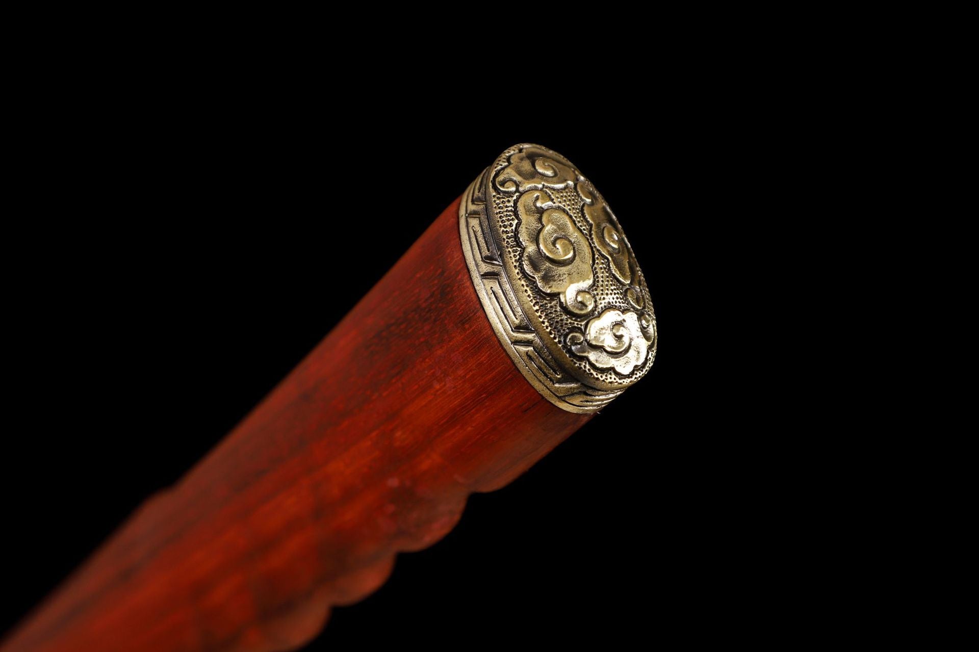 Closeup of the kashira of a red rosewood katana tsuka with intricate gold carvings and a smooth finish.