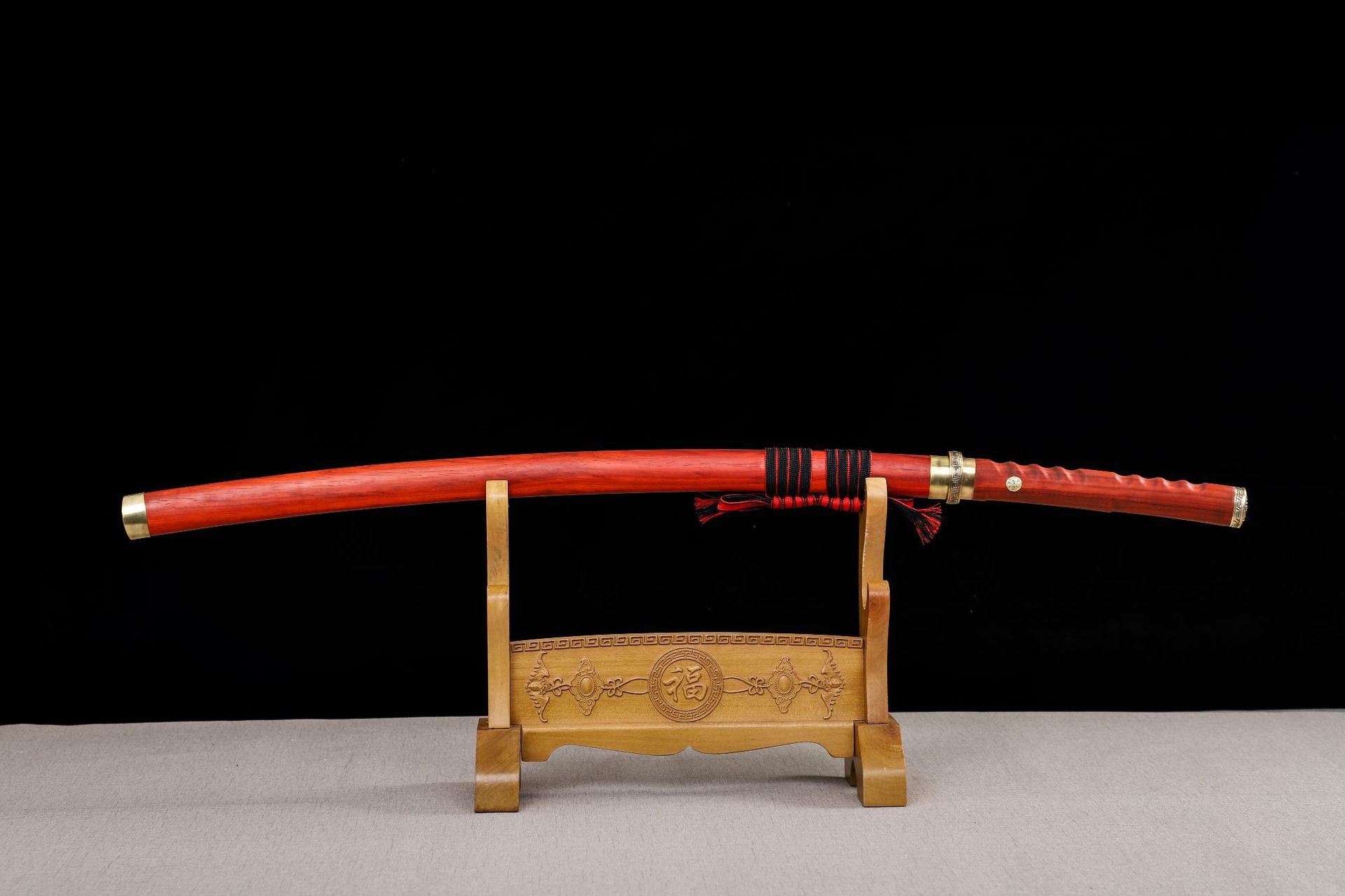 Japanese katana sword with a red rosewood scabbard and red sageo, displayed on an intricately carved wooden stand.