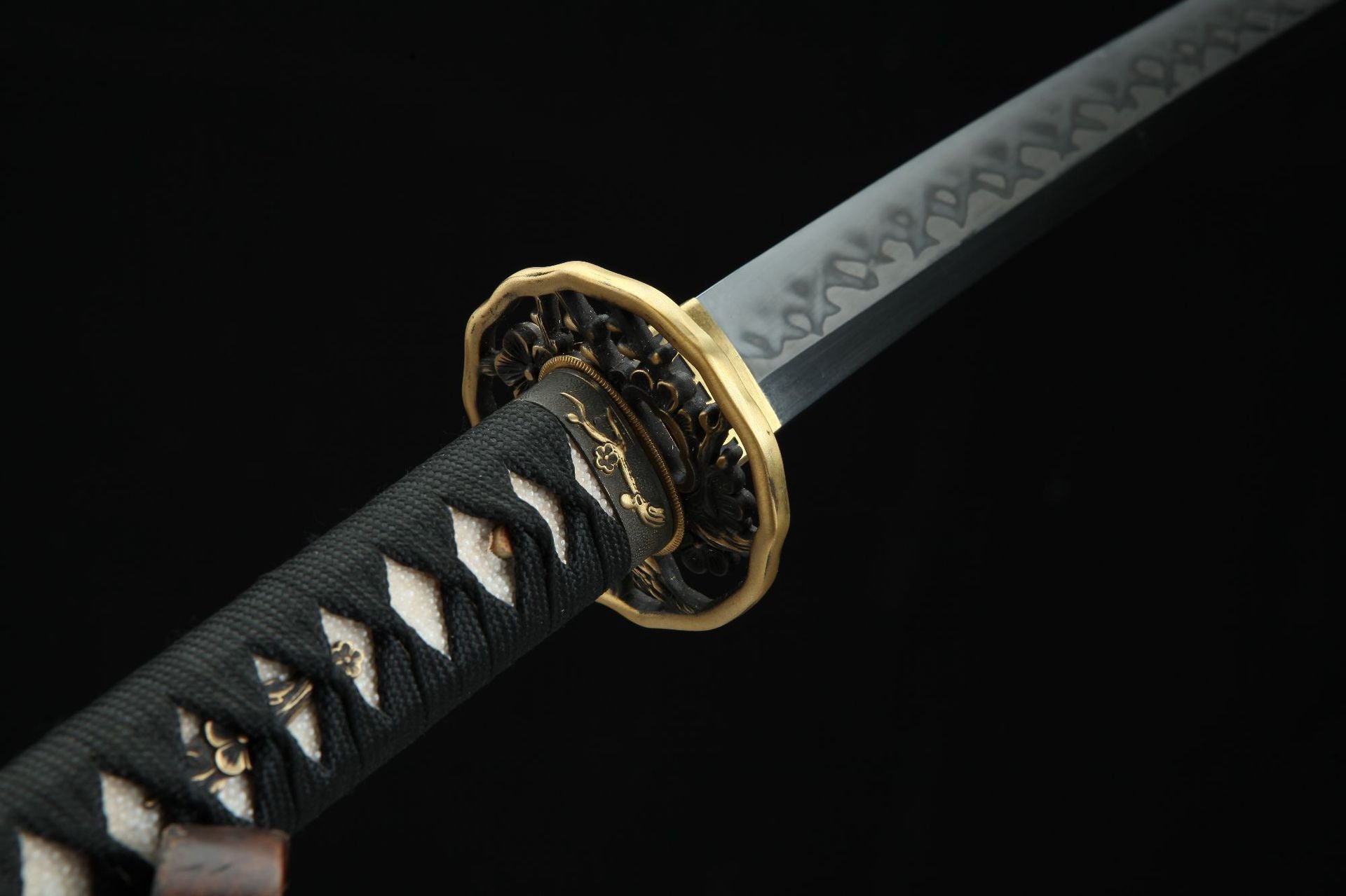 Closeup of the Sakura X katana showing the intricately designed guard with cherry blossom carving and the handle wrapped in black and red ito.