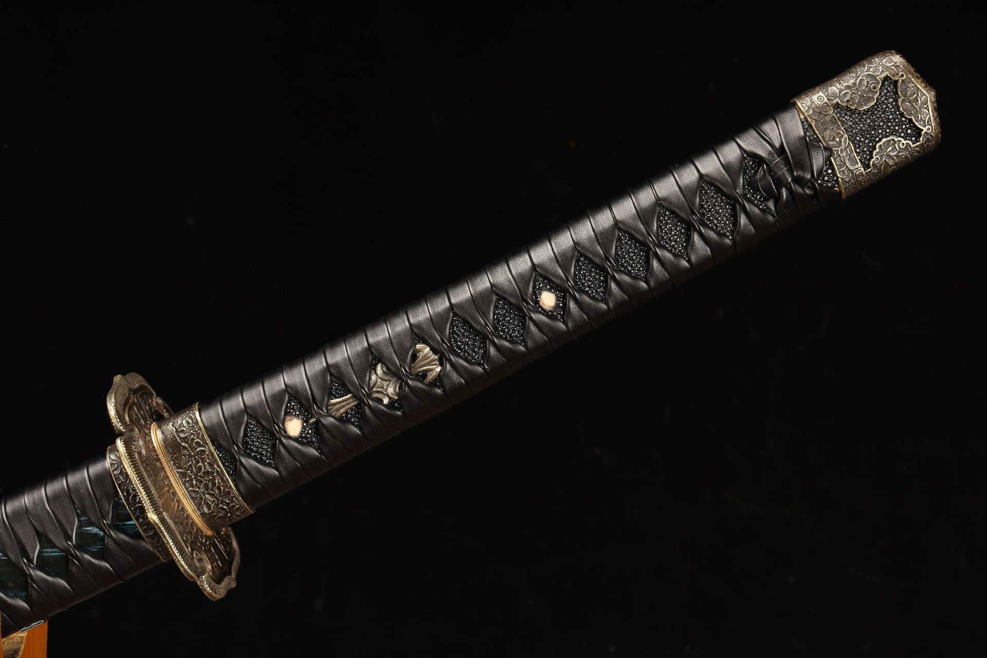 Closeup of a tachi hilt with black leather wrapping and intricate gold accents.