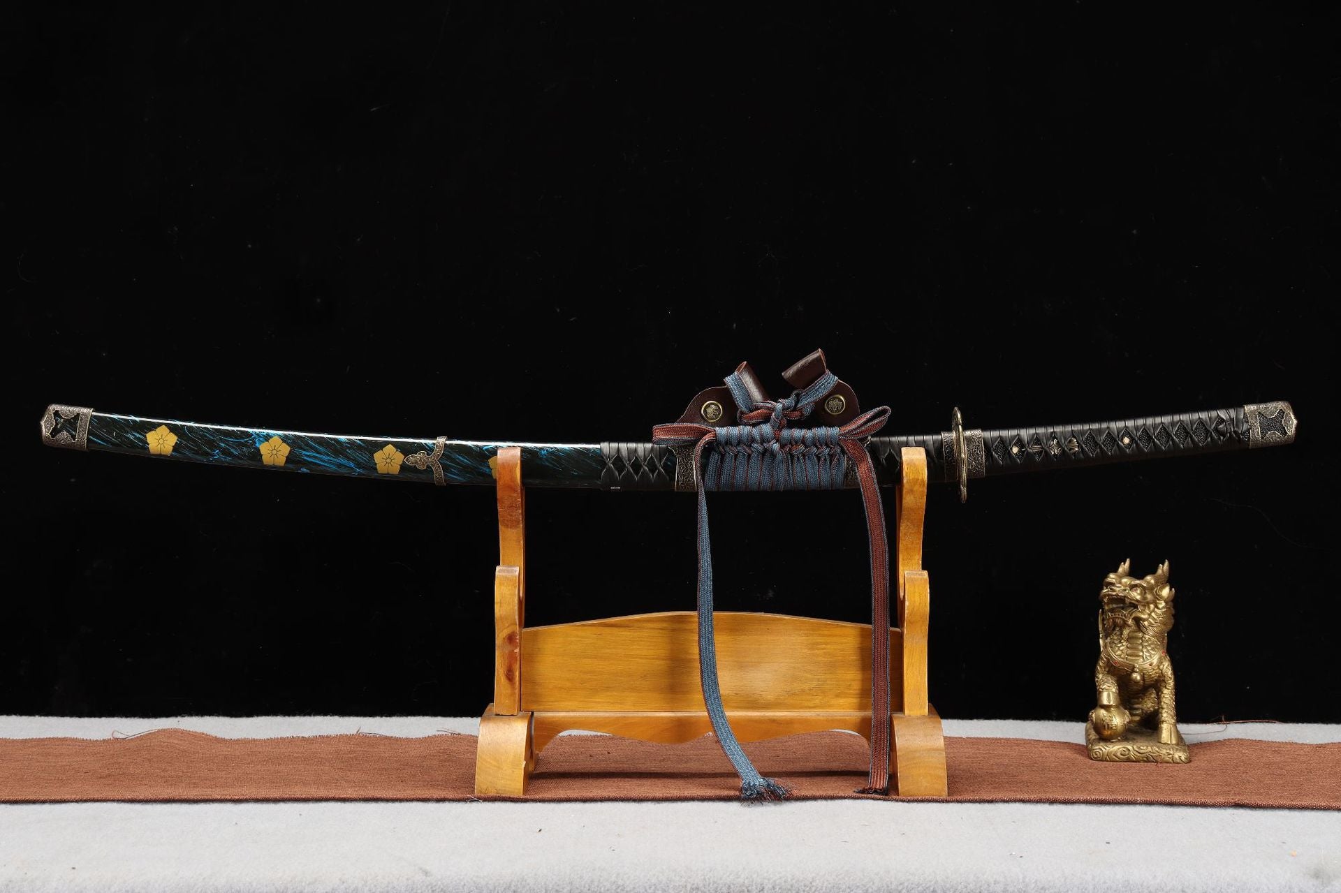 Tachi displayed on a wooden stand with a blue and gold scabbard and decorative sageo wrapping.