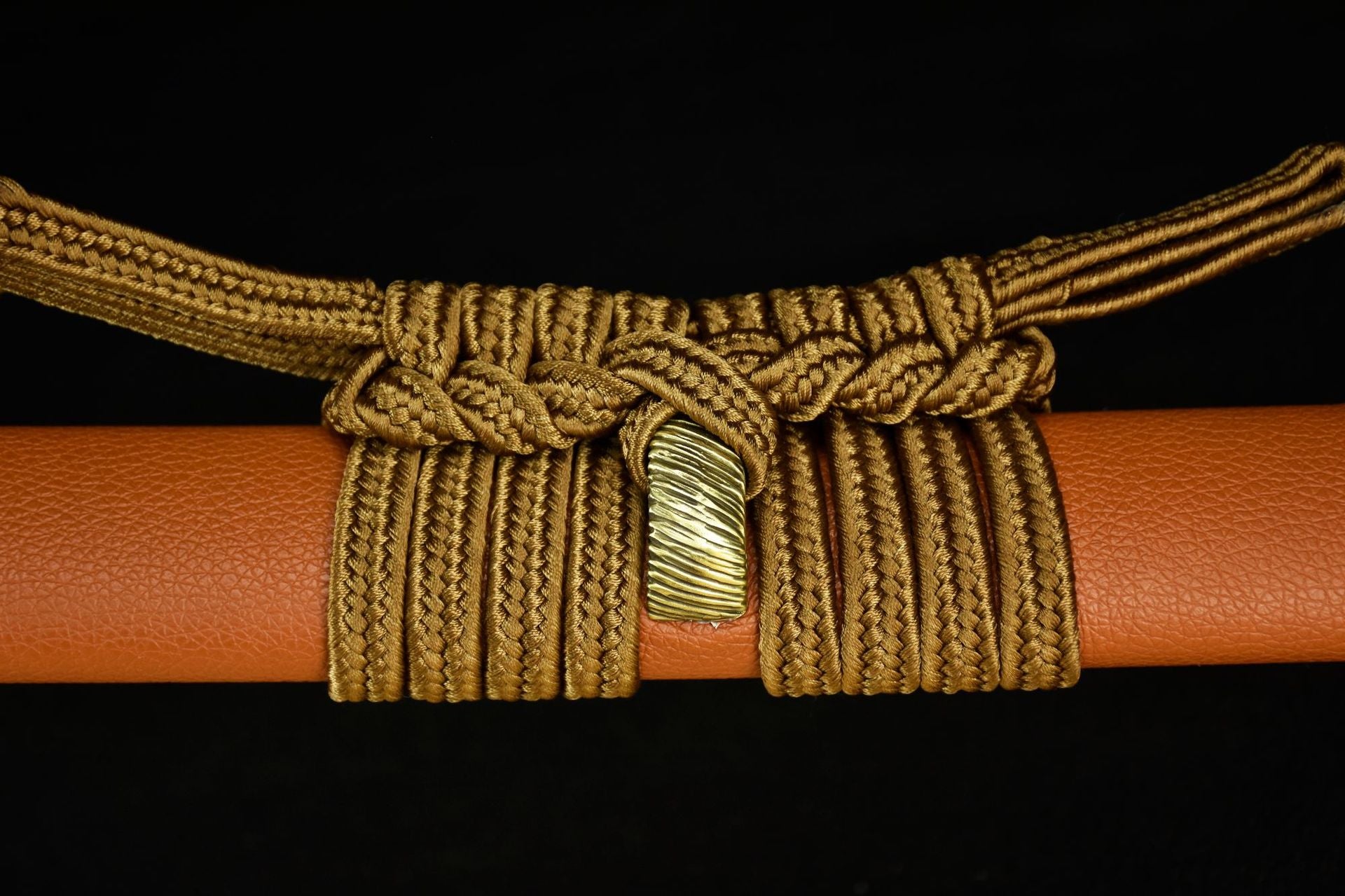 Close-up of a tan scabbard wrapped with intricate decorative cord and a brass kurigata, showcasing fine detail and traditional design.
