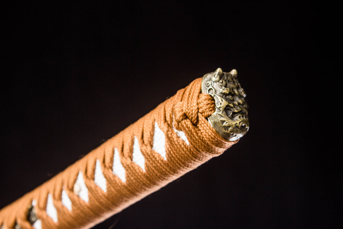 Close-up of the Sakura in Gold Katana’s orange handle wrap and sculpted metal end cap