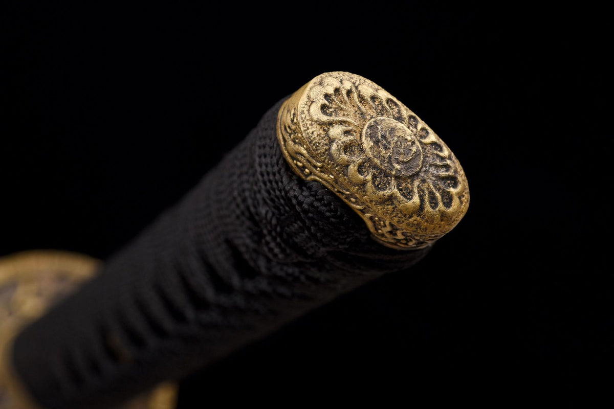 Close-up of the Twin Dragons Katana’s dark handle wrap and antique carved gold-toned end fitting