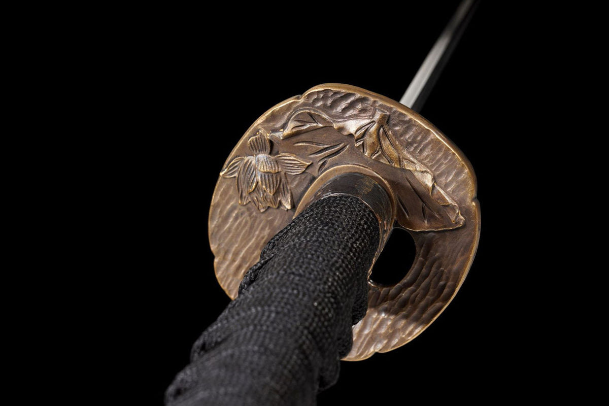 Close view of the bronze-toned carved tsuba and black tsuka wrap