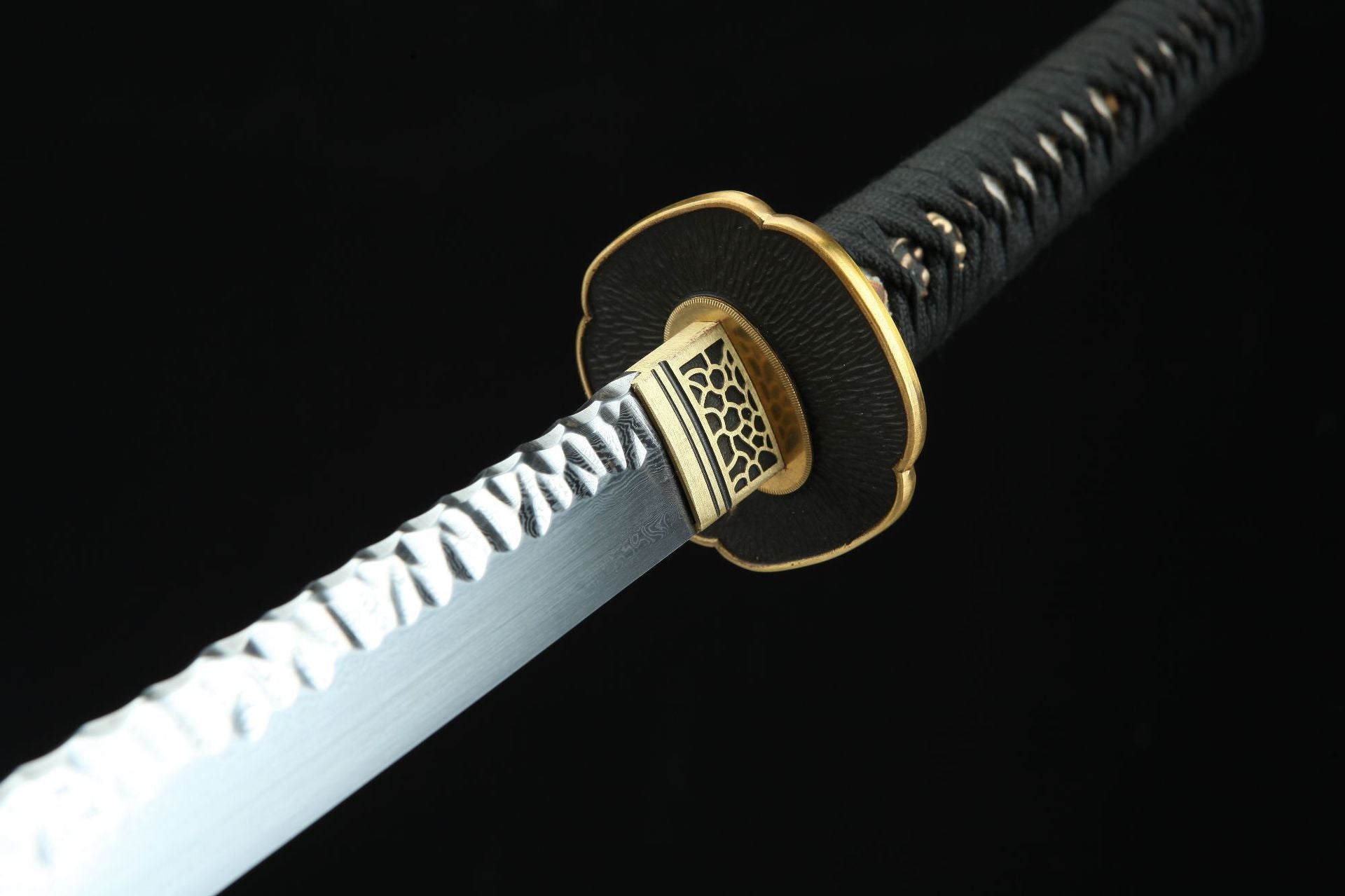 Close-up of a handcrafted Damascus steel blade with a brass tsuba and black handle wrap.