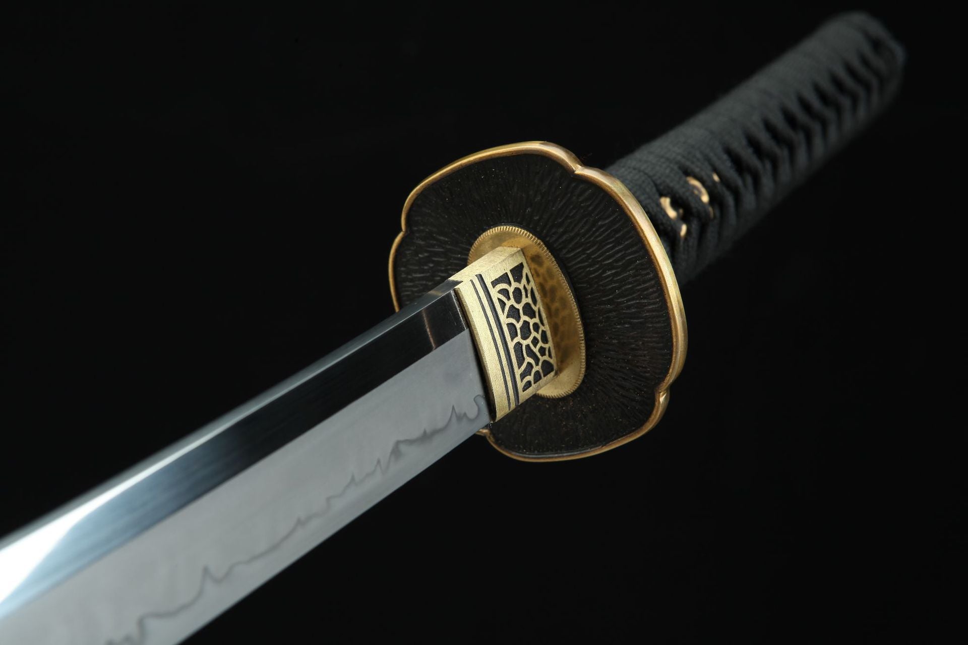 Close-up of the Magatama katana blade and tsuba, featuring intricate gold accents and a hamon pattern on the polished blade.