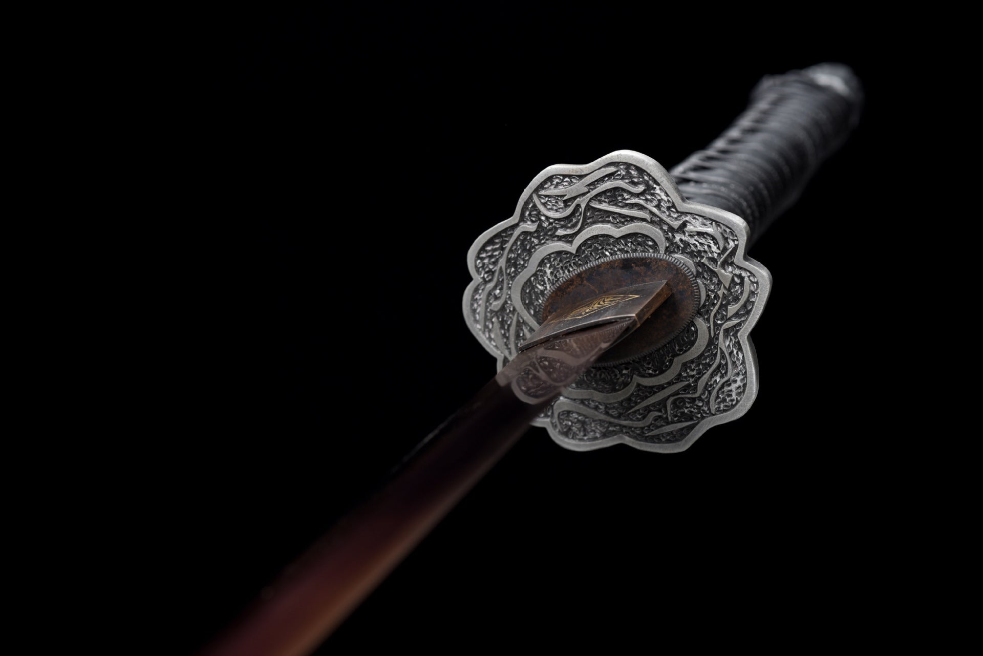 The silver, aged tsuba of the Mortal Blade from Sekiro: Shadows Die Twice, engraved with intricate patterns.