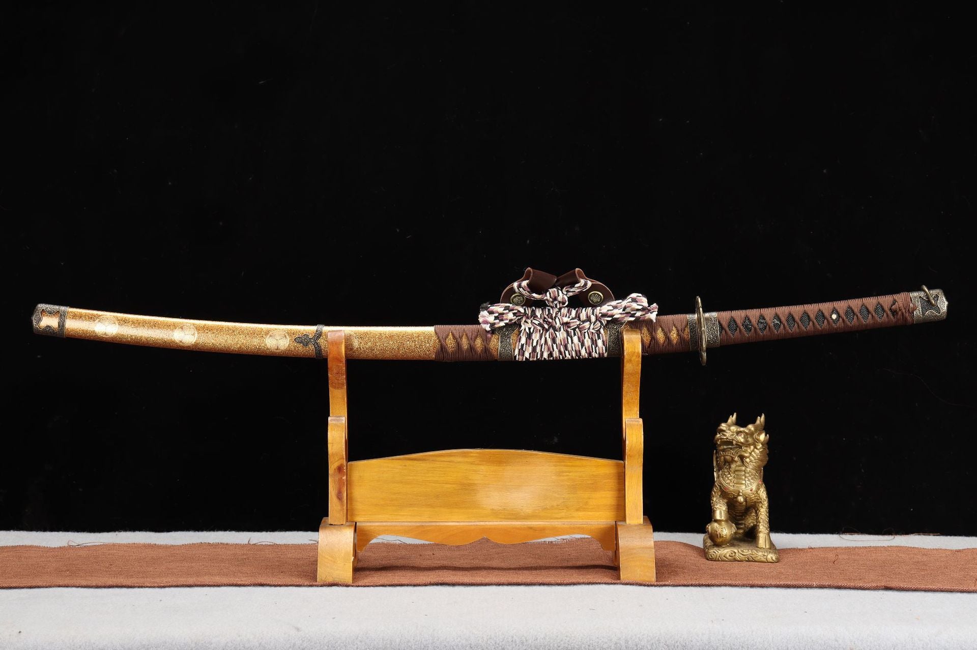 Nobunaga Tachi sword displayed on a wooden stand with a decorative scabbard and a brass statue, showcasing its elegant craftsmanship.
