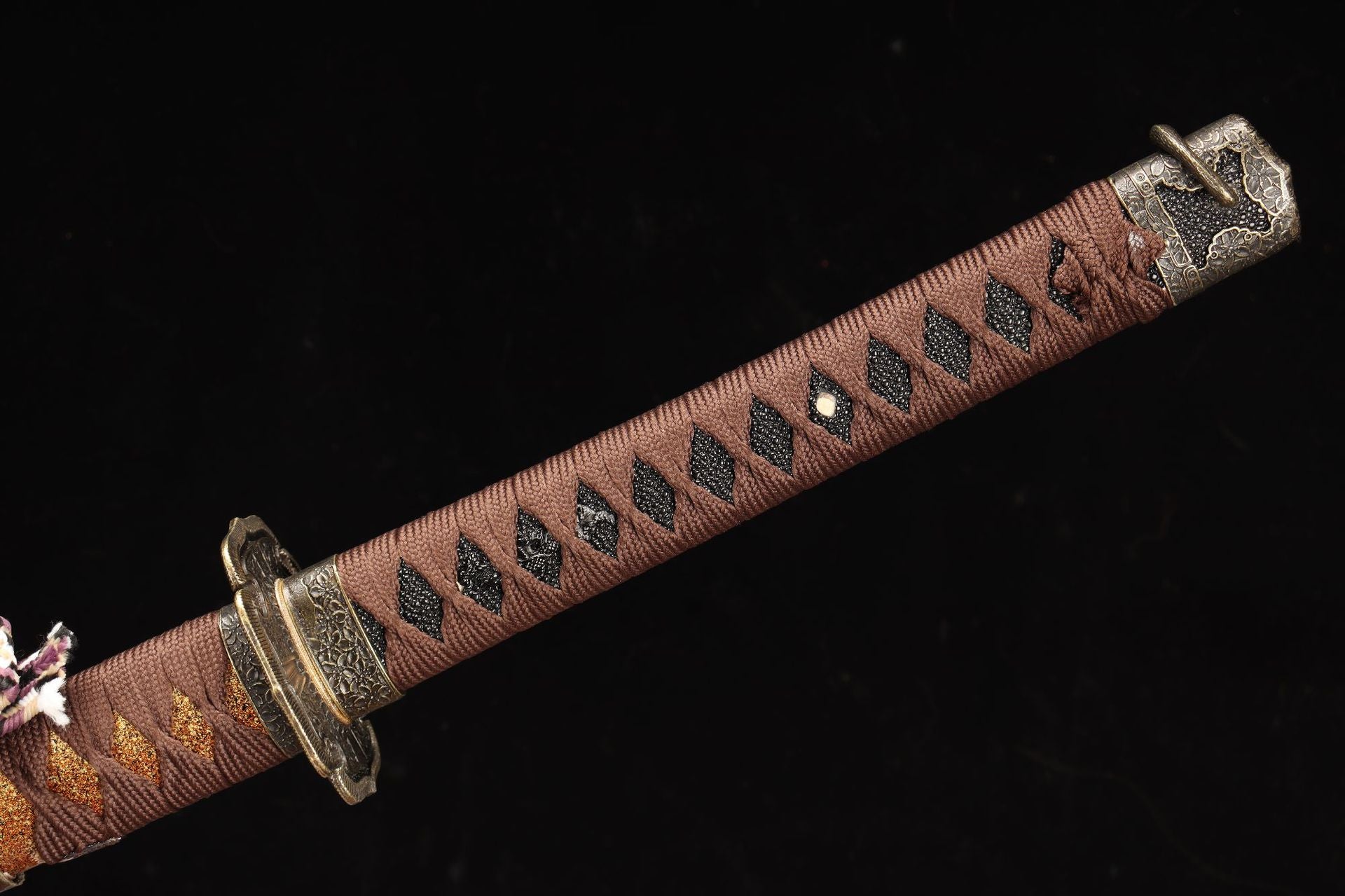 Close-up of the Nobunaga Tachi sword handle, featuring a traditional tsuka wrapped in brown silk cord with black ray skin accents and intricate metal fittings.