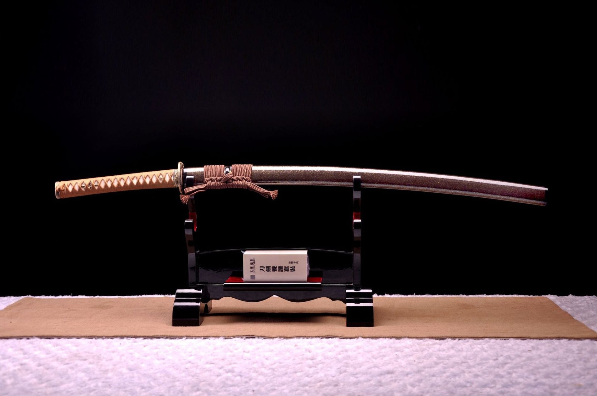 A samurai sword with its sheath displayed on a black stand, showcasing traditional craftsmanship and detailed wrapping.