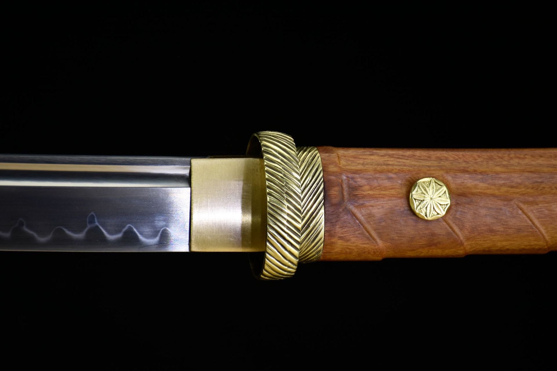 Close-up of a katana blade with a polished brass habaki, elegant wooden handle, and intricate decorative fittings.