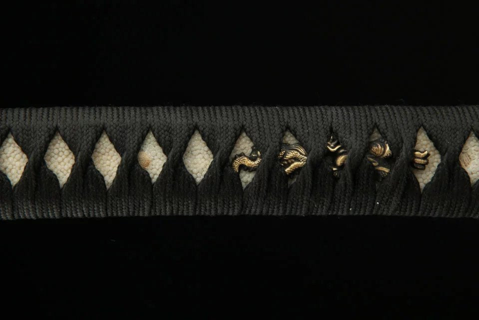 Close-up of a katana handle wrapped in white ray skin, featuring komainu menuki details, highlighting intricate Japanese craftsmanship.